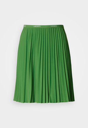 Green pleated skirt with an elastic waistband featuring the Lacoste logo. Made of smooth material, it has distinct vertical folds and a knee-length cut.