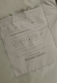 Polo Club-ydertøjsmærke, der viser ultralys, skræddersyet pasform, ekstra varm, vandafvisende, genbrugt polyesterfunktioner på beige stof.