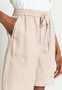 Shorts en lin beige avec une taille élastique munie d'un cordon de serrage, des poches latérales et une coupe décontractée au toucher doux.