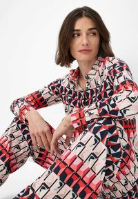 Camicia a maniche lunghe con bottoni e pantaloni abbinati in un motivo geometrico di rosso, rosa, nero e bianco. Tessuto morbido, design aderente.