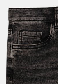 Close-up van zwarte denim jeans die de voorzak en kleine muntenzak toont met zichtbare stiksels en stoftextuur.