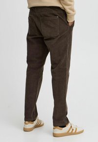 Pantaloni in corduroy marroni con taglio dritto, dotati di due tasche posteriori. Abbinati a sneaker bianche con dettagli beige.
