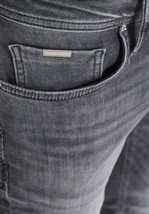 Primo piano della tasca di jeans in denim grigio scuro con una piccola etichetta metallica rettangolare attaccata vicino al bordo della tasca.