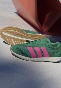 Zelené športové topánky z jemného a syntetického materiálu. Majú jasne ružové pruhy, štruktúrovaný povrch a gumenú podrážku.