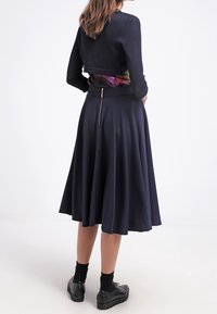 Top in maglia blu navy con un design accorciato abbinato a una morbida gonna lunghezza ginocchio. Presenta una fascia in vita floreale multicolore e chiusura con zip.