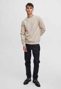 Beige sweatshirt with a crew neck and long sleeves, paired with dark denim jeans. The outfit features a smooth texture and simple design.