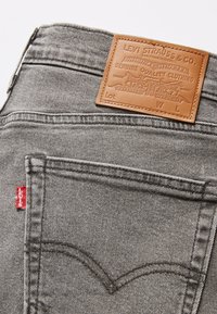 Jeans in denim grigio con una toppa posteriore in pelle che presenta testo e disegni in rilievo. Include un'etichetta rossa Levi's sul lato.
