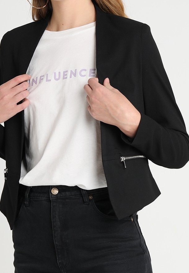 Musta bleiseri, jossa on istuva leikkaus ja vetoketjuyksityiskohtia, päällä valkoinen t-paita, jossa on vaaleanpunaisella kirjoitettu sana "INFLUENCE".