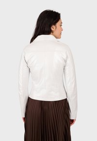 Bijela kožna jakna s uskim dizajnom, strukturiranim ramenima i vidljivim šavovima, u kombinaciji s naboranom smeškom suknjom.