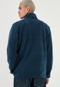 Giacca in pile blu navy con colletto alto, texture morbida e maniche lunghe. Presenta una vestibilità comoda e un design semplice.