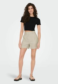 Černý crop top a béžové šortky s vysokým pasem. Šortky mají sklady a hladký povrch. Obuv je s pásky a má plochou podrážku.