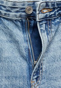 Jeans de mezclilla azul con cremallera metálica parcialmente desabrochada y cierre de botón metálico encima de un ojal cosido.