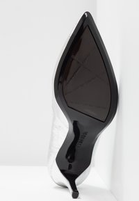 Chaussure à talon stiletto à bout pointu avec une semelle noire et une tige blanche texturée, présentée semelle vers le haut sur un fond blanc.
