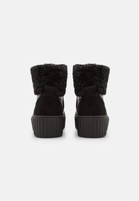 Bottines noires à la cheville avec un bord en fausse fourrure texturée, un corps en suède lisse, et une semelle en caoutchouc rainurée. Tirette arrière pour plus de commodité.