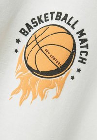 Tejido blanco con un diseño gráfico que presenta un balón de baloncesto naranja y llamas. El texto dice "PARTIDO DE BALONCESTO" en negro. Incluye estrellas notables.
