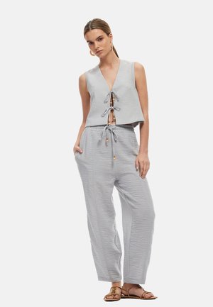Jasnoszara, bezrękawnikowa bluzka crop top z wiązaniami z przodu i akcentami z drewnianych koralików, zestawiona z luźnymi, spodniami na gumce w tym samym fakturowanym materiale.