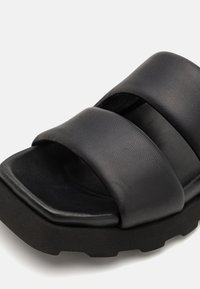 Svart halksandaler med två breda, texturerade remmar och en formad fotbädd. Sula är tjock med ett robust mönster för grepp.