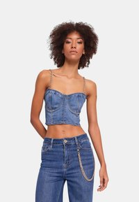 Top corto in denim con scollatura dritta, spalline a catena e dettagli delle cuciture. Abbinato a jeans in denim a vita alta con un accento a catena.