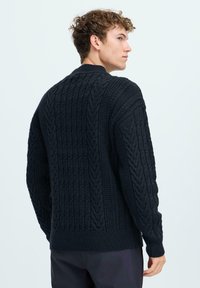 Un pull foncé avec un motif tricoté texturé et des designs en cable. Manches et ourlet côtelés, encolure ronde. Style simple et décontracté.