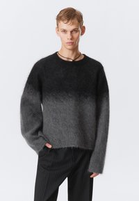 Un pull en dégradé de tons gris, fabriqu�é en matériau doux et duveteux. Il présente un col rond et des manches longues, associé à un pantalon noir à rayures.