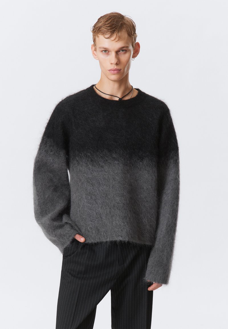 Un pull en dégradé de tons gris, fabriqué en matériau doux et duveteux. Il présente un col rond et des manches longues, associé à un pantalon noir à rayures.