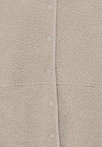 Tissu polaire beige doux avec une surface texturée et bouclée, et une rangée de boutons-pression ronds le long d'une couture centrale.