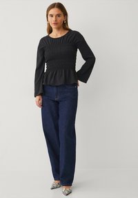Zwarte longsleeve top met smock-lichaam en peplum zoom, gecombineerd met hoge taille donkerblauwe jeans en puntige slangenhuid hakken.