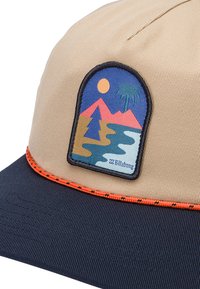 Kaki caps med en marineblå skygge, med en fargerik lapp av fjell og palmetre. Utsmykket med oransje detaljer langs kanten av skyggen.