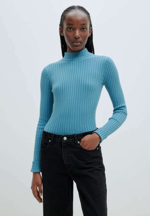 Light blue ribbed long-sleeve top with a high neck and fitted design, paired with high-waisted black jeans featuring silver hardware.