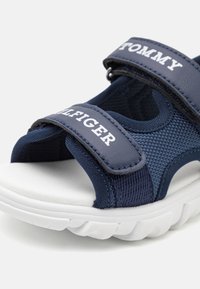 Modré nylonové sandály s nastavitelnými popruhy, bílými logy a texturovanou bílou podrážkou s vlnkovým vzorem, vhodné pro každodenní nošení.