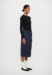 Jūras spēku zila svārku kleita ar viļņotiem detalizējumiem sānos, apvienota ar melnu garām piedurknēm topu, baltām zeķēm un melniem kurpēm. Gluda, pielāgota auduma tekstūra.