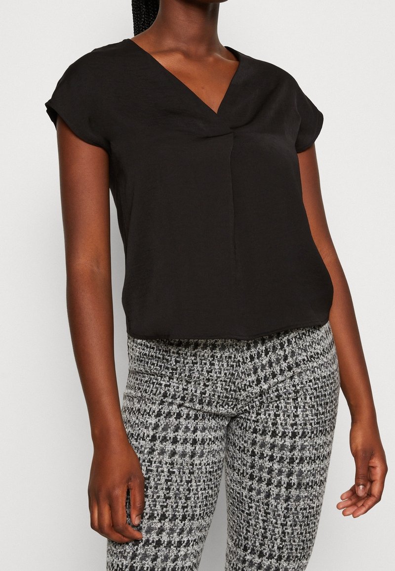 Top corto a maniche corte nero con scollo a V e dettagli di pieghe sottili, abbinato a leggings grigi texturizzati con un motivo a scacchi.