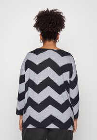 Grijs en zwart zigzagpatroon sweater met driekwartmouwen en een ontspannen pasvorm, gemaakt van een zacht breimateriaal.