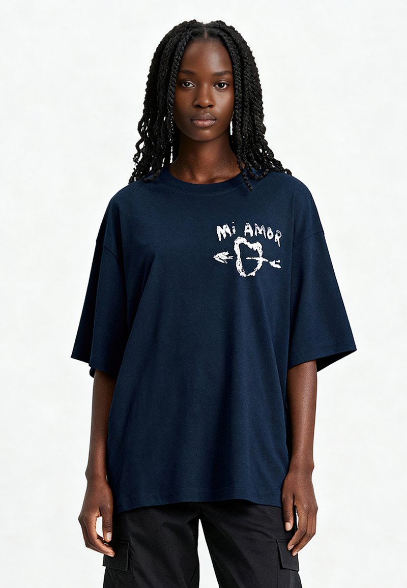 T-shirt en coton bleu marine à coupe décontractée, arborant un texte graphique "Mi Amor" et un design de cœur avec des flèches à l'avant.