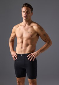 Black fitted athletic shorts made of stretchy fabric with a smooth texture. Features a logo on the waistband and a mid-length design.