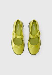 Green glossy Mary Jane-style shoes with a round toe, adjustable buckle strap, and black rubber outsole. Smooth material with a shiny finish.