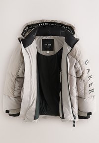 Puffermantel in hellbeige mit gestepptem Muster, schwarzen Akzenten, Innenbranding und zwei Reißverschlusstaschen.