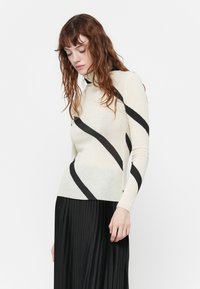 Maglietta crema a maniche lunghe con strisce diagonali nere, collo alto, texture morbida. Abbinata a una gonna plissettata nera per creare contrasto.