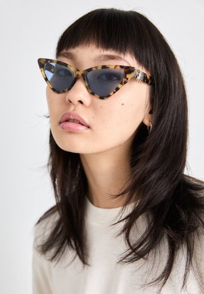 Katzenaugen-Sonnenbrille mit einem Schildpatt-Rahmen und dunklen Gläsern. Verfügt über metallische Akzente an den Bügeln, die ein markantes Design zeigen.
