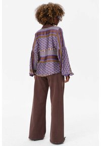 Paarse blouse met lange mouwen en een patroonontwerp, voorzien van brede uitlopende mouwen en een relaxte pasvorm, gecombineerd met bruine wijde broekspijpen.