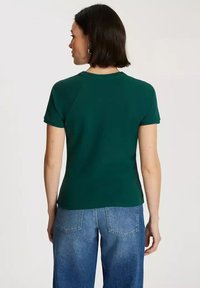 Ciemnozielona koszulka z krótkim rękawem o dopasowanym kroju i okrągłym dekolcie, wykonana z miękkiej bawełny. Posiada rękawy raglanowe oraz gładką fakturę.