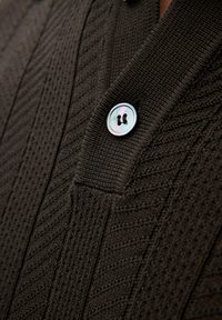 Brun stickad tröja med V-halsdesign, texturerade mönster och en rund, iriserande knapp med två hål.