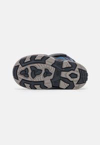 La suela de las zapatillas deportivas para niños presenta una base de goma gris con patrones de tracción negro profundo y un diseño curvado que proporciona flexibilidad y agarre.