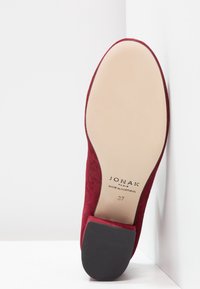 Chaussure en daim rouge avec une surface lisse, un bout arrondi et un talon en caoutchouc noir. Présente le logo sur la semelle intérieure et fabriquée au Portugal. Taille 37.