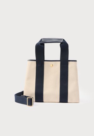 Sac fourre-tout en toile beige avec deux larges anses bleu marine, prise en cuir sur le dessus, bouton doré, et bandoulière amovible bleu marine avec boucle dorée.