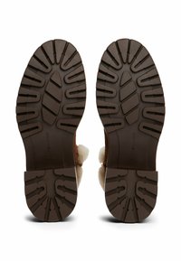 Suelas de goma marrón, estriadas, con patrones de agarre texturizados y huellas pronunciadas, diseñadas para proporcionar tracción y durabilidad en el calzado.