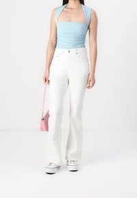 Světle modrý vyšívaný krátký top se širokými ramínky, v kombinaci s bílými džínami s vysokým pasem a rozšířenými nohavicemi a bílými teniskami. Růžová kabelka doplňuje vzhled.