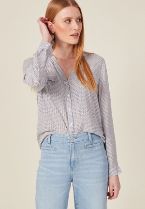Camicia bianca con piccoli motivi rossi e blu, maniche lunghe e vestibilità rilassata, abbinata a jeans in denim azzurro chiaro con tasche anteriori.