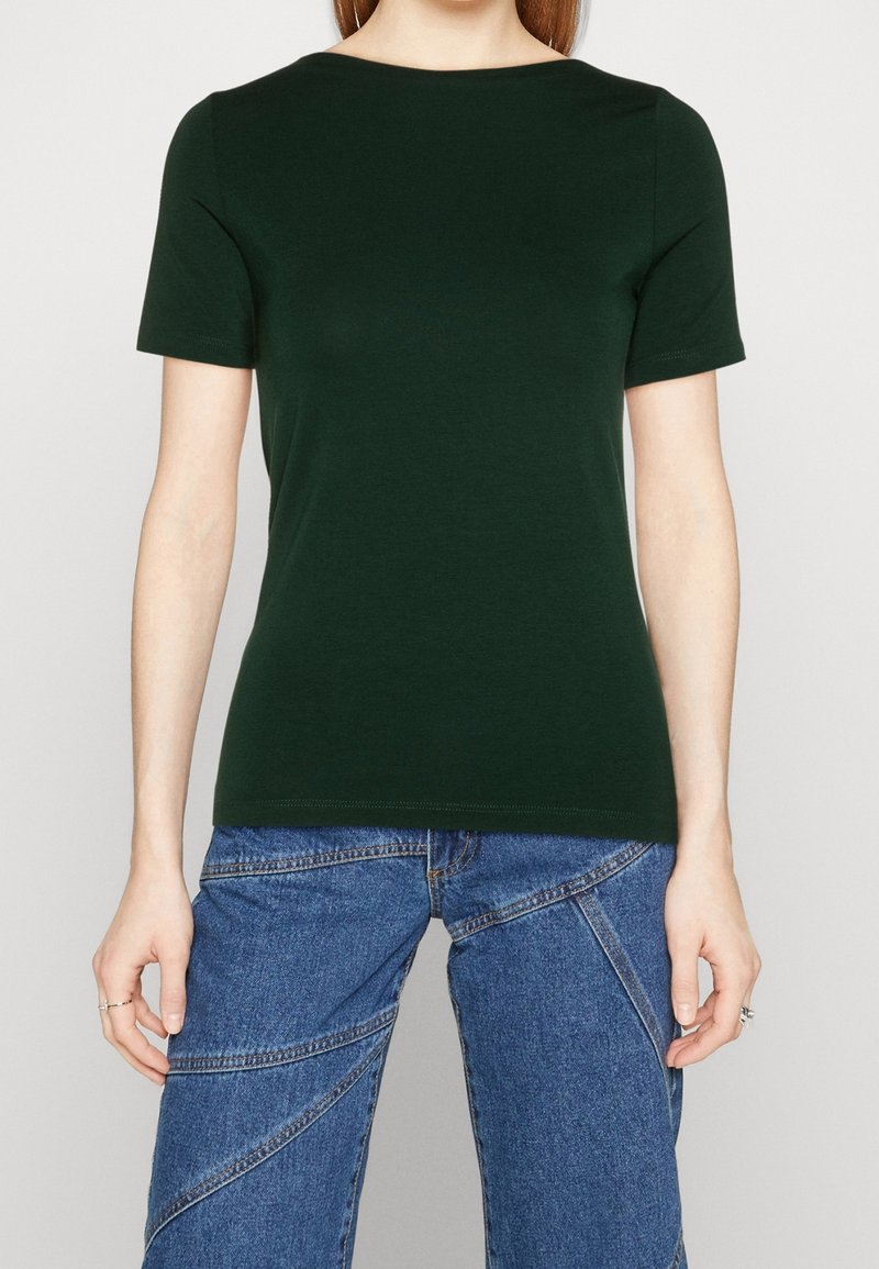 Camiseta verde de manga corta hecha de tela suave, con un escote redondo y un diseño ajustado, combinada con unos jeans de mezclilla azul con costuras únicas.