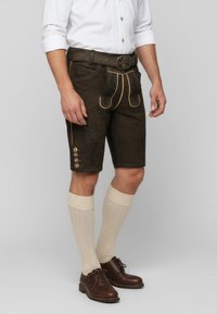 Braune Ledershorts mit goldenen Nähten, dekorativer Stickerei und Knopfakzenten. Tragen Sie sie mit cremefarbenen, knielangen Socken und braunen Schuhen.